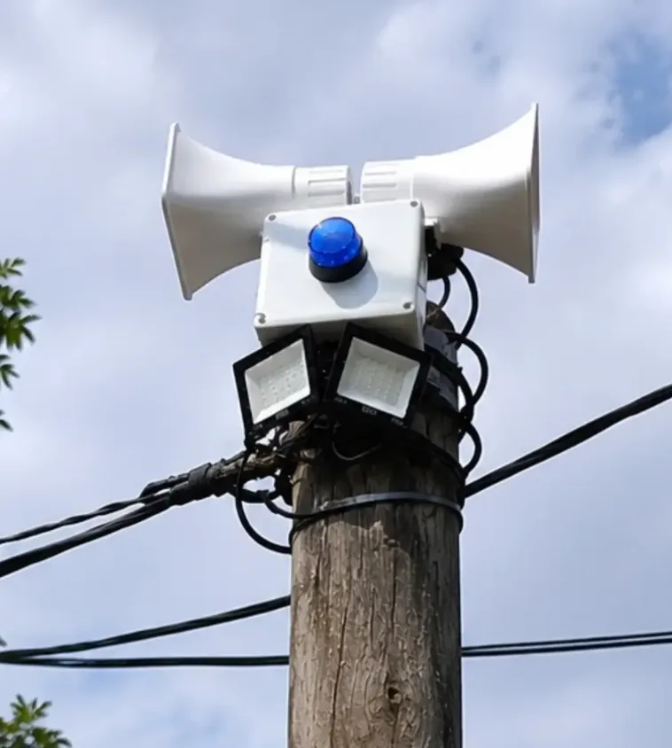Alarma vecinal montada en un poste con doble sirena, baliza y reflectores.